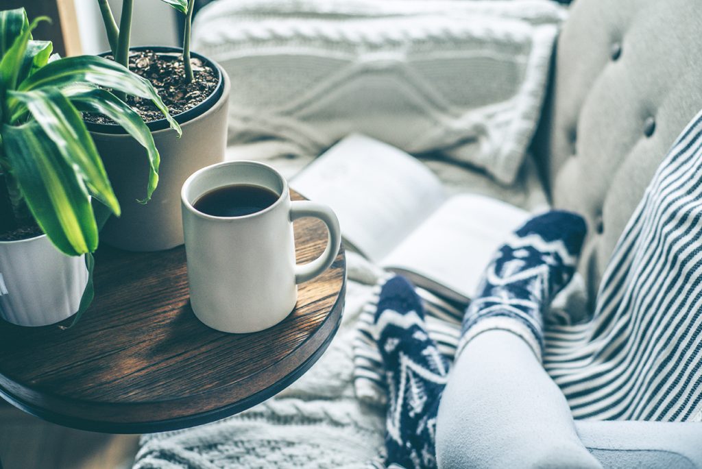 Young woman enjoying coffee and relaxing on a sofa with a book